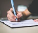 Close-up of hand writing in notebook using a blue pen, focus on creativity.